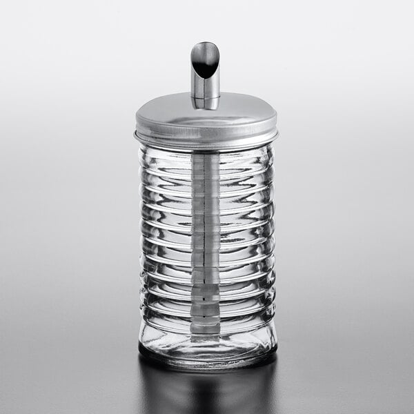 A glass sugar pourer with a beehive design and a stainless steel pour spout top.