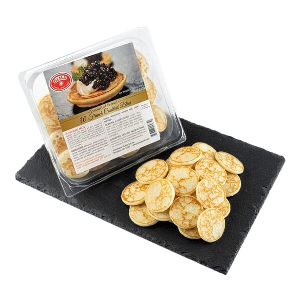 A package of OLMA Mini French Blini, each about 1 inch in diameter, with several blini displayed on a black slate serving tray.