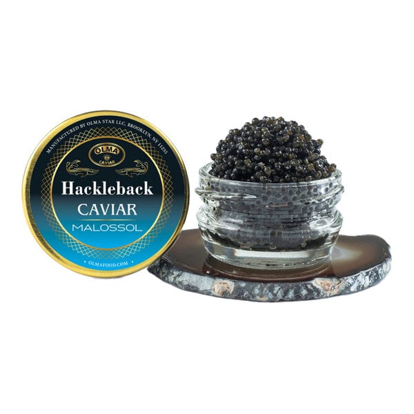 A small glass jar filled with black Hackleback caviar next to a labeled tin lid.