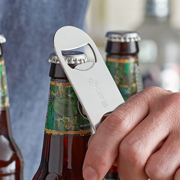 A stainless steel flat bottle opener being used to open a capped glass bottle.