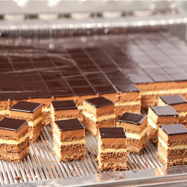 A metal cutting frame used for slicing layered desserts into uniform 2-inch squares.