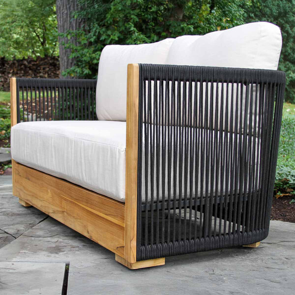 A modern outdoor love seat featuring black rope sides, a teak wood frame, and white Sunbrella cushions.