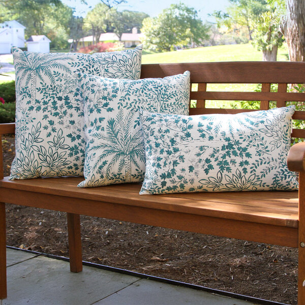 A set of three square and rectangular outdoor pillows with a tropical jade leaf pattern, displayed on a wooden bench.