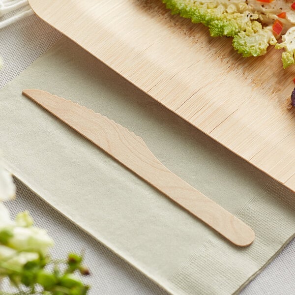 A compostable wooden knife placed on a napkin next to a wooden plate with food.