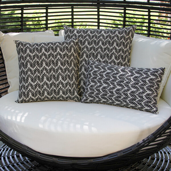 A set of black and white leaf-patterned lumbar pillows displayed on a round outdoor seat.