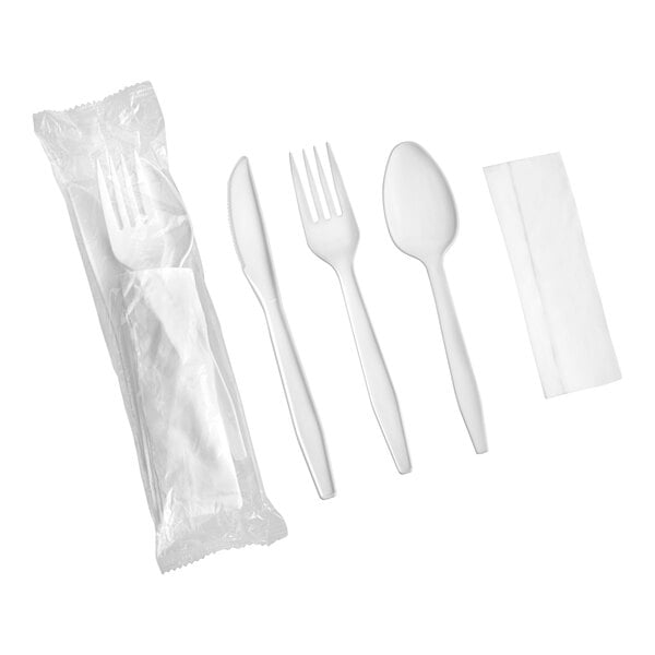 A set of white heavy weight plastic cutlery including a knife, fork, spoon, and a napkin, with one set shown in its packaging.