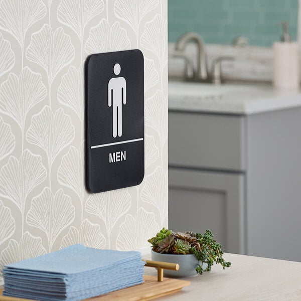 A black and white plastic men's restroom sign with braille mounted on a wall.