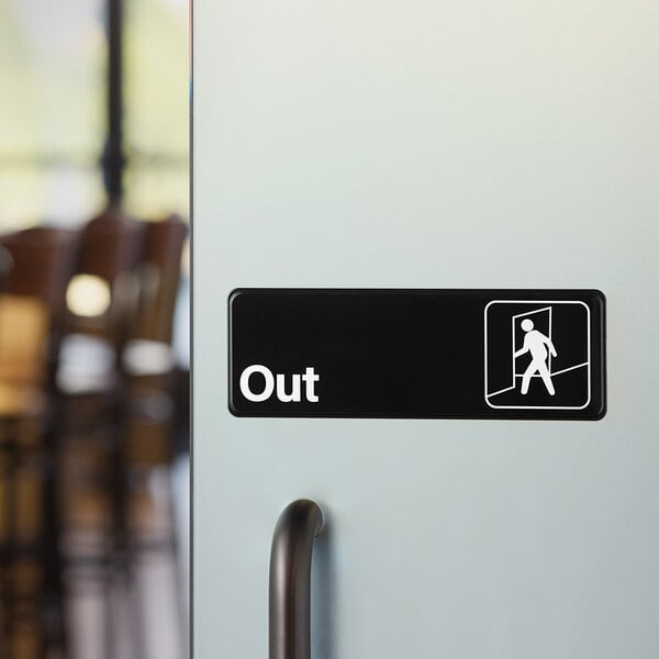 A black and white plastic sign reading 'Out' with an exit symbol, mounted on a door.