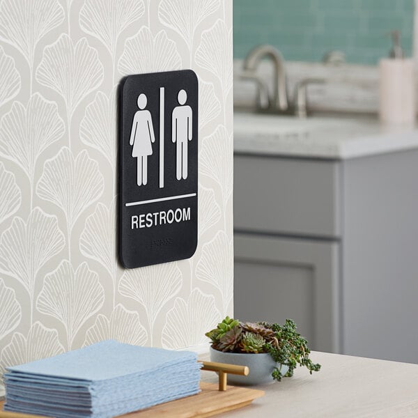A black and white plastic unisex restroom sign with braille mounted on a wall.