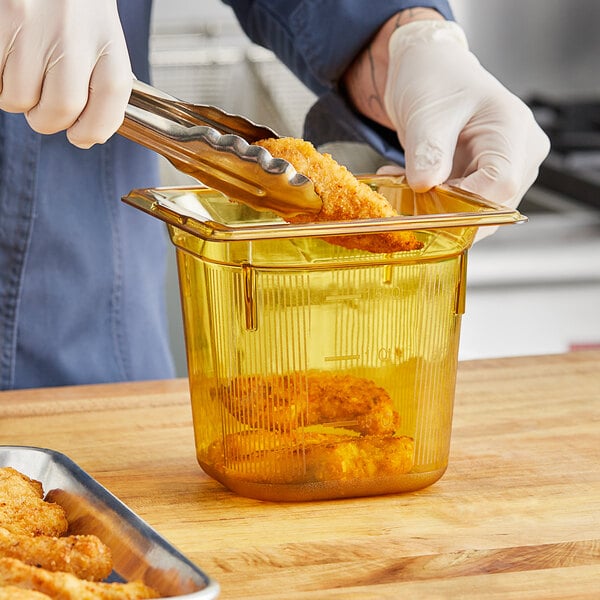 A person using tongs to put food in a Vollrath amber plastic food pan.