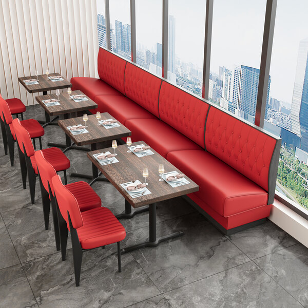 A bright red upholstered double booth with a button-tufted back and walnut finishes, positioned alongside dining tables in a restaurant setting.