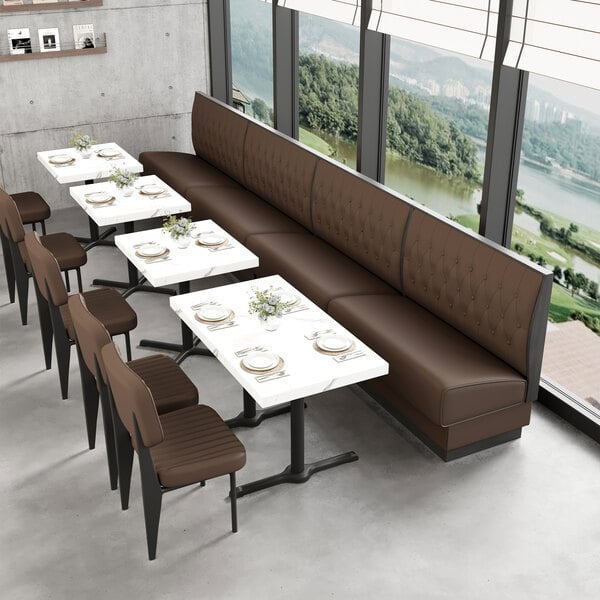 A long brown upholstered single booth with a button-tufted back and walnut finishes, positioned alongside white tables and brown chairs in a modern dining area.