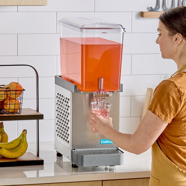 A single-bowl refrigerated beverage dispenser with a clear container holding red liquid, being used to fill a glass.