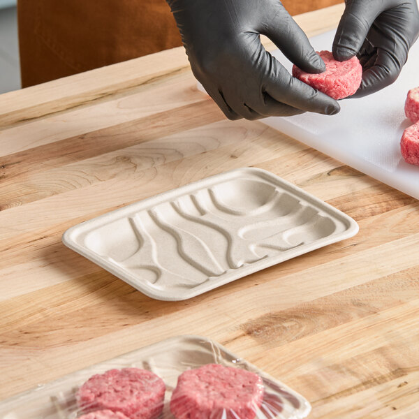 A rectangular compostable fiber meat tray on a wooden surface.