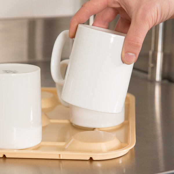 A beige cup stacker tray holding several white mugs, with a hand lifting one mug.