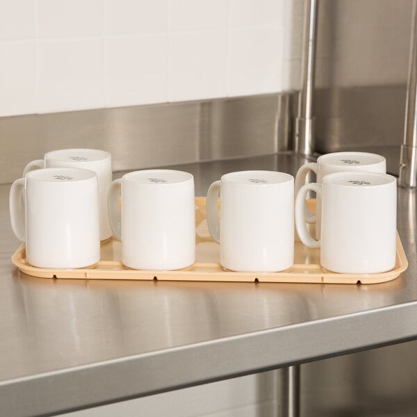 A beige cup stacker holding eight white ceramic mugs, placed on a stainless steel countertop.