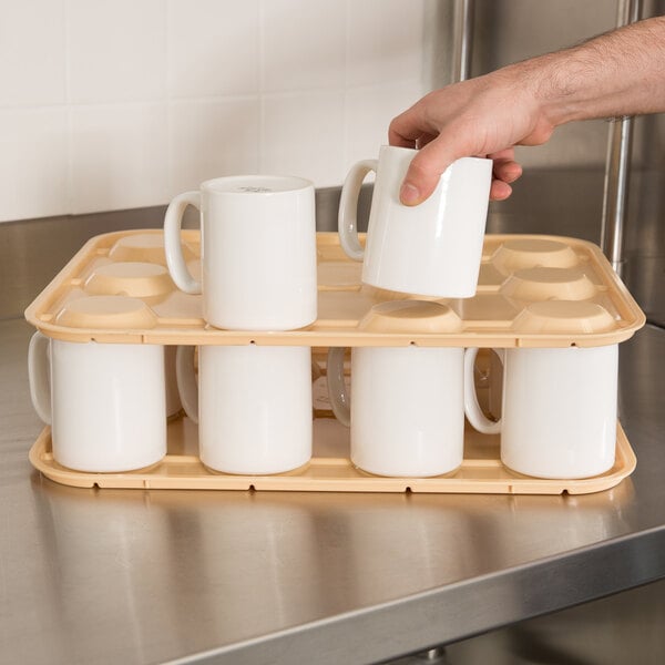 A beige cup stacker holding multiple white mugs on a stainless steel countertop.