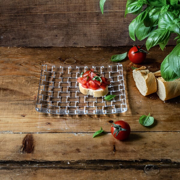 A square glass plate with a woven pattern, holding a piece of bruschetta, displayed on a wooden surface.