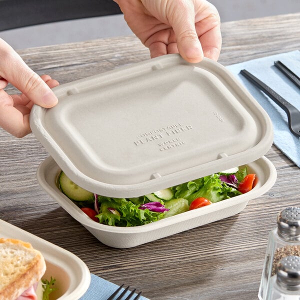 A compostable fiber lid being placed on a rectangular food container filled with salad.