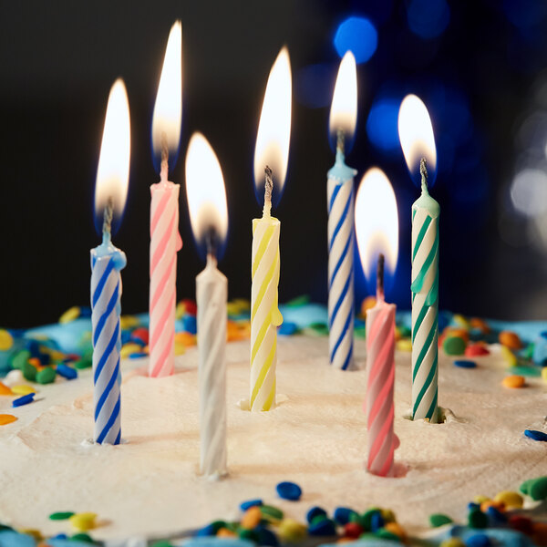 A group of lit multi-colored striped birthday candles on a frosted cake with confetti sprinkles.