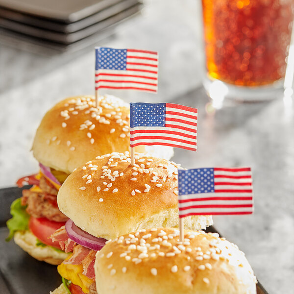 A set of sesame seed hamburger sliders each topped with a small American flag food pick.