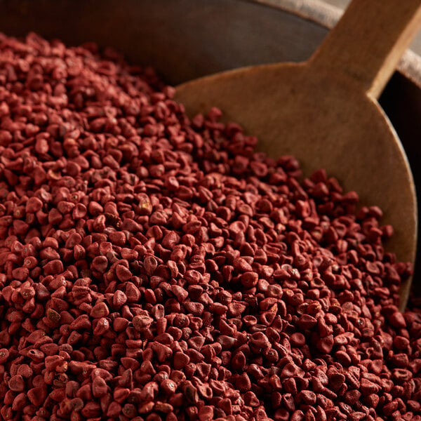 A close-up of a pile of annatto seeds with a wooden scoop.