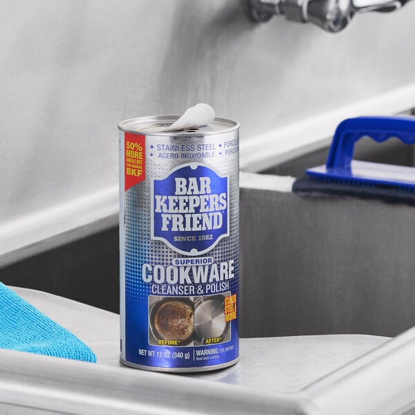 A canister of Bar Keepers Friend Superior Cookware 12 oz. cleansing and polishing powder placed on a stainless steel countertop near a sink.