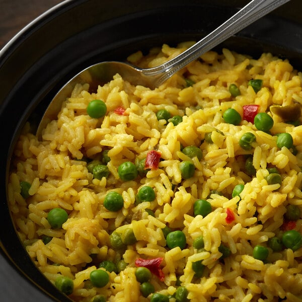 A bowl of yellow rice mixed with green peas and red bell peppers, served with a spoon.