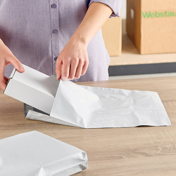 A white expandable polyethylene mailer with a tamper-evident adhesive closure being used to package a box.