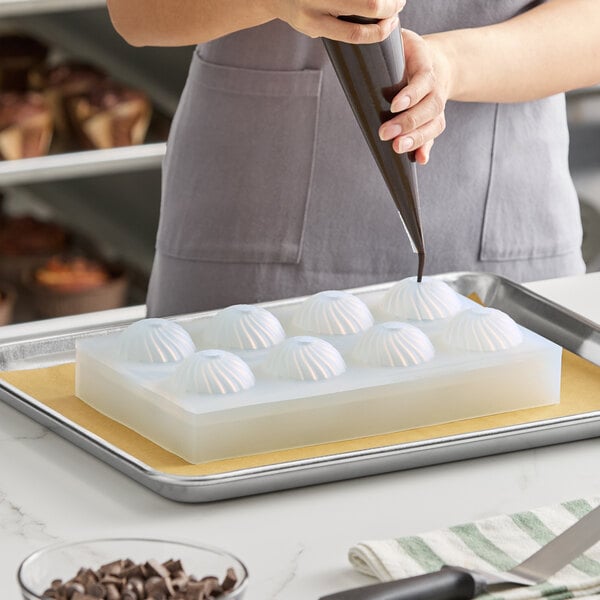 A silicone chocolate mold with eight dome-shaped compartments being filled with chocolate.