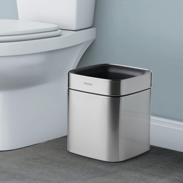 A stainless steel square wastebasket with a 2-gallon capacity placed next to a toilet.
