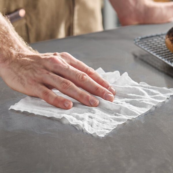A hand is using a white wipe to clean a smooth, gray surface.