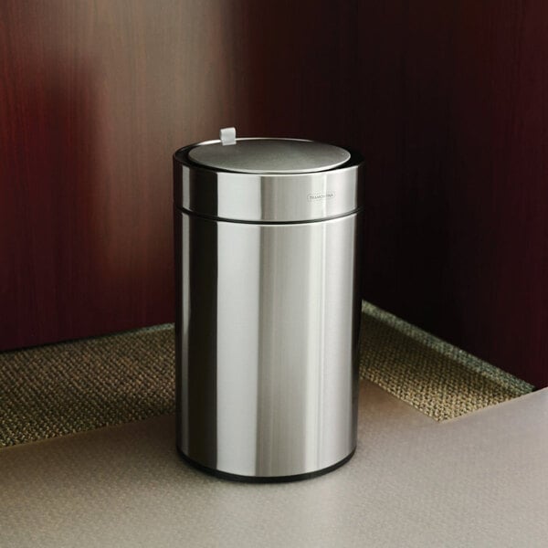 A stainless steel round wastebasket with an automatic lid.