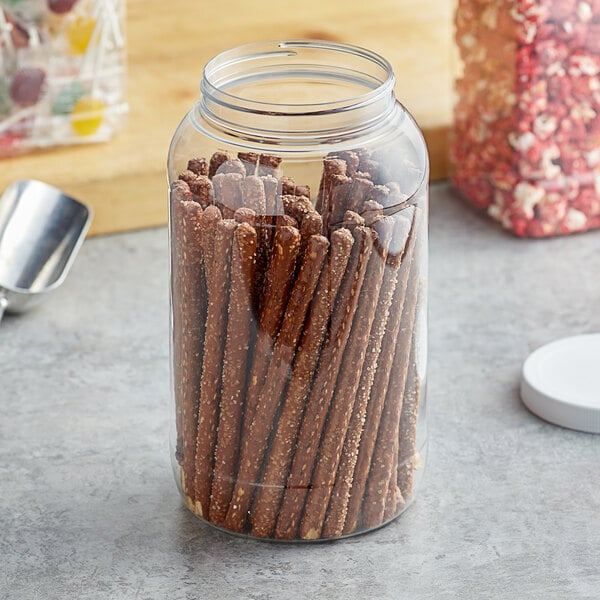 A clear round plastic jar filled with pretzel sticks.