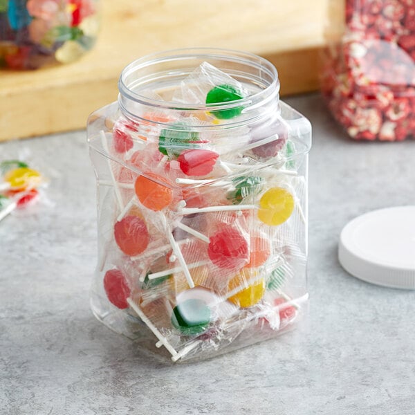 A clear square plastic jar filled with assorted wrapped lollipops.