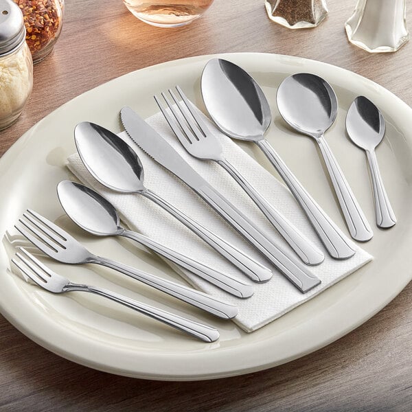 A set of stainless steel dinner and dessert spoons displayed on a plate with other cutlery.