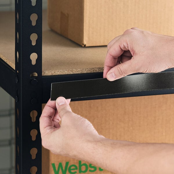 A person applying a black slip strip label holder to the edge of a metal shelving unit.