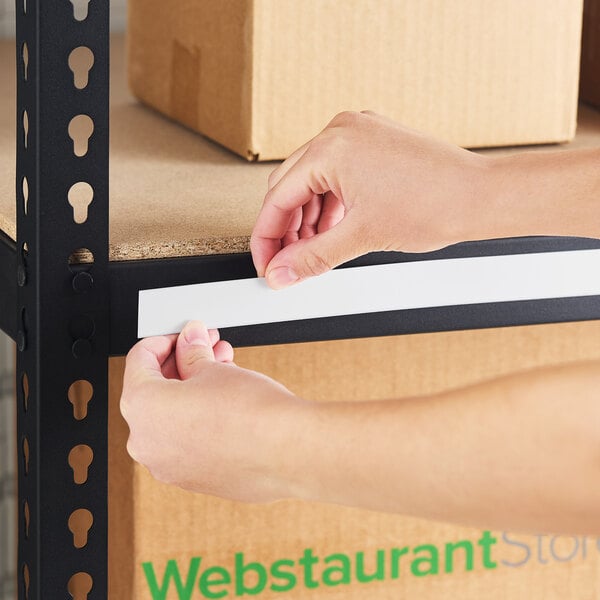A person placing a white slip strip label holder onto the edge of a black metal shelf.