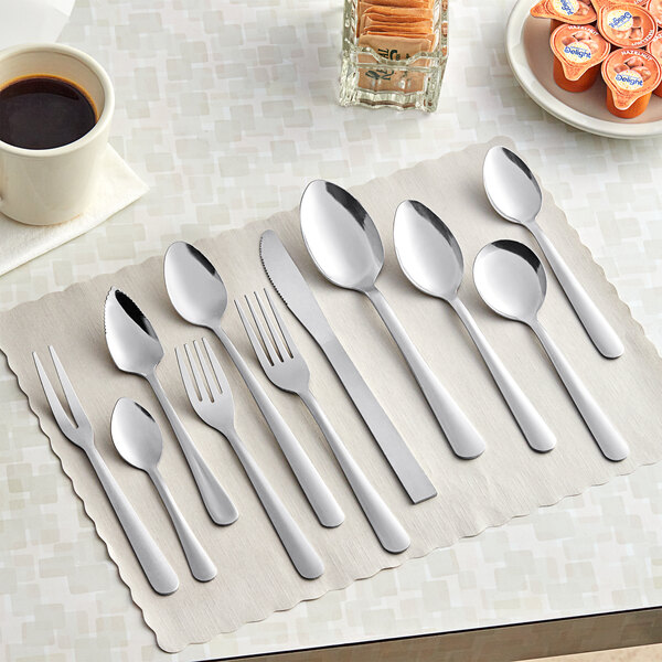 A stainless steel tablespoon or serving spoon placed among other flatware on a placemat.