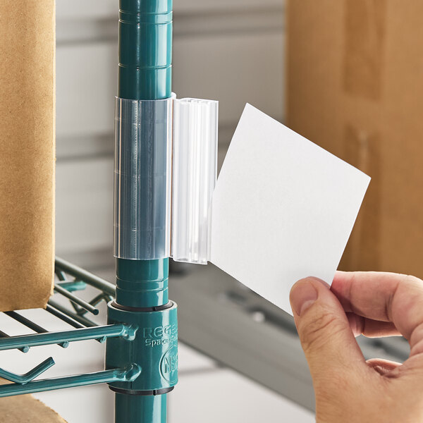 A clear plastic post grip label holder attached to a metal shelving post, with a hand inserting a label.
