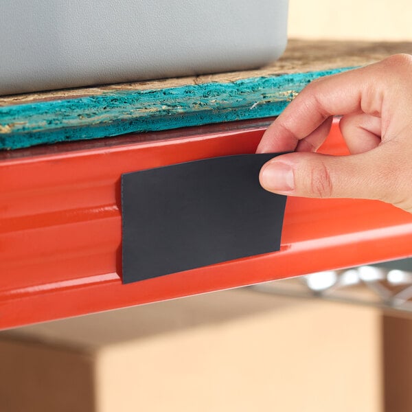 A hand placing a black magnetic label holder onto a red steel shelf.