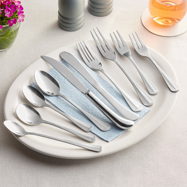 A set of stainless steel medium weight teaspoons displayed on a plate with other cutlery.