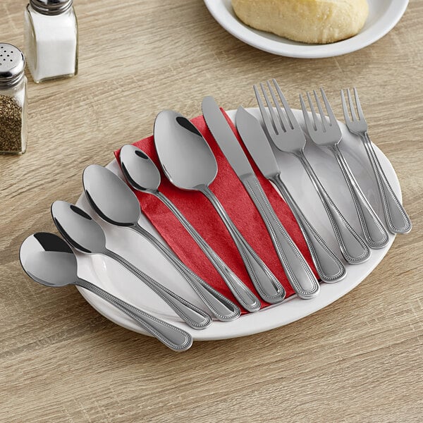 A set of stainless steel dinner knives, spoons, and forks arranged on a white plate with a red napkin.