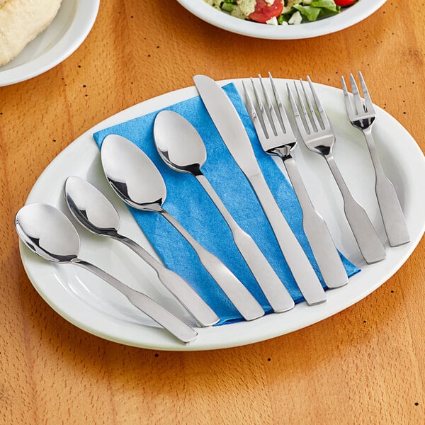 A set of stainless steel flatware including forks, knives, and spoons arranged on a white plate with a blue napkin.