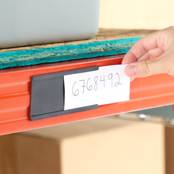 A black heavy-duty magnetic label or card holder attached to a metal shelf with a handwritten card inserted.