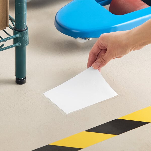 A clear adhesive floor label holder measuring 4 by 6 inches being applied to a floor.