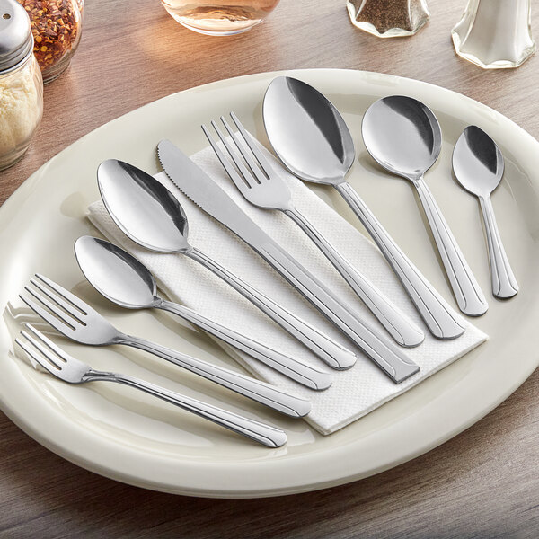 A set of stainless steel medium weight teaspoons displayed on a plate with other cutlery.