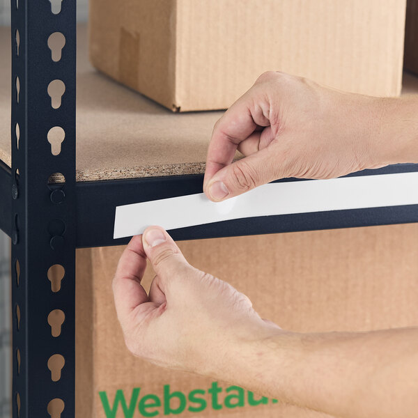 A person applying a white slip strip label holder to the edge of a metal shelving unit.