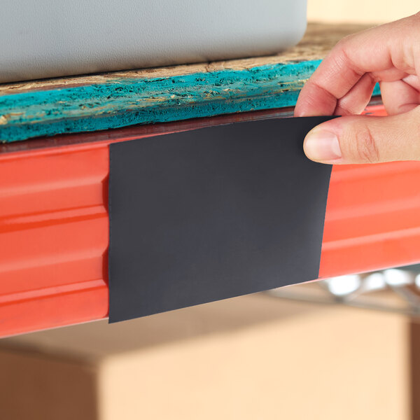 A hand placing a black pre-scored magnetic label holder onto a red steel shelving unit.