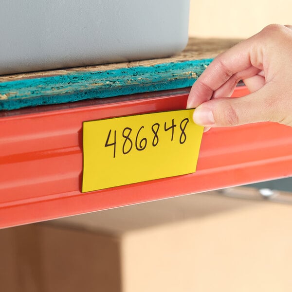 A yellow magnetic write-on label being applied to a metal shelf.